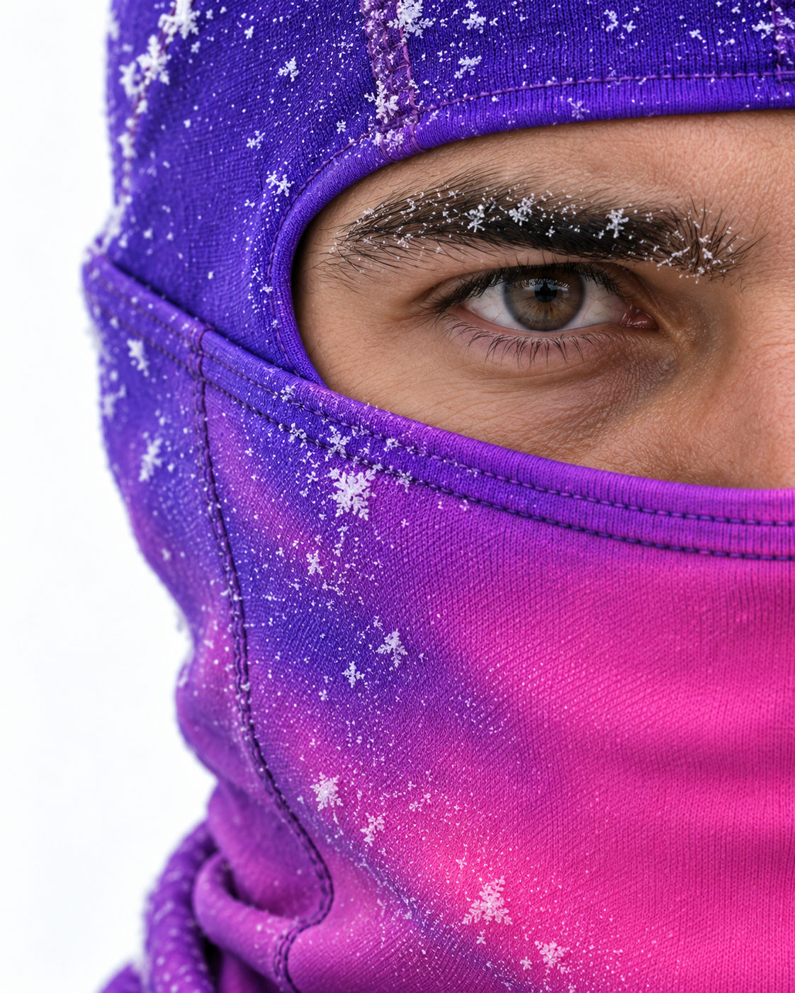Frontal half-face macro of violet-to-pink balaclava fabric, with snow crystals on the eyebrow against white